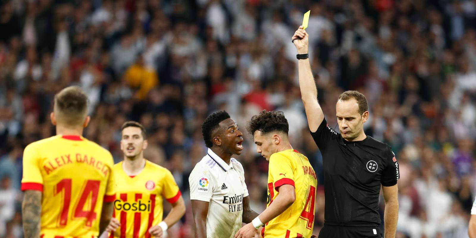 L'àrbitre del Madrid-Girona, Melero López, ensenya la targeta groga a Arnau Martínez, mentre Vinicius Jr fa una protesta | Europa Press